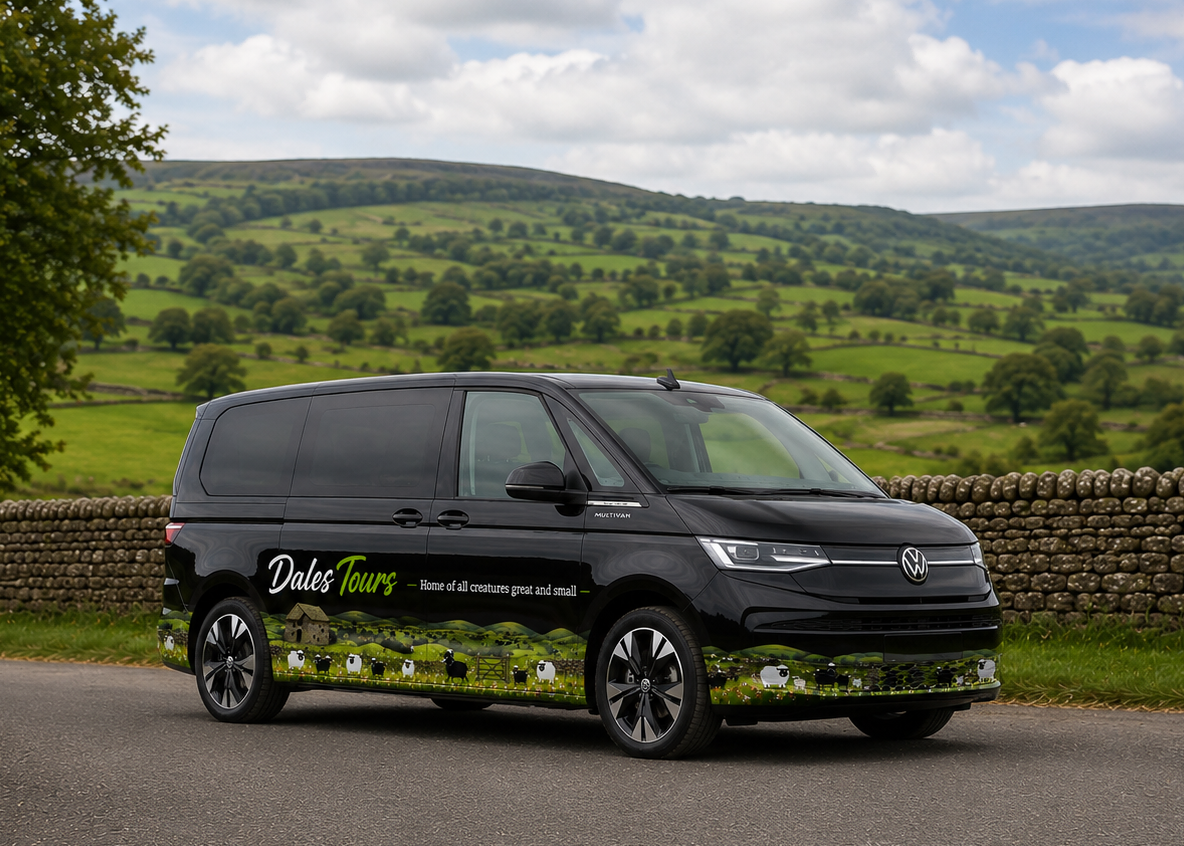 A black Volkswagen Transporter van with 'Dales Tours' branding and a scenic green hillside wrap, parked on a country road with a stone wall and rolling green hills in the background.